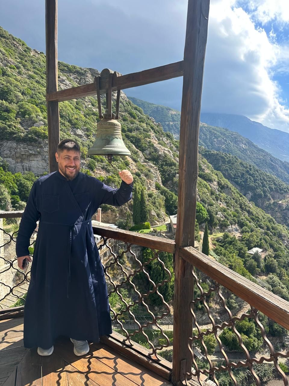 Father Pavel ringing the bell at an Athonite monastery, mountains behind him