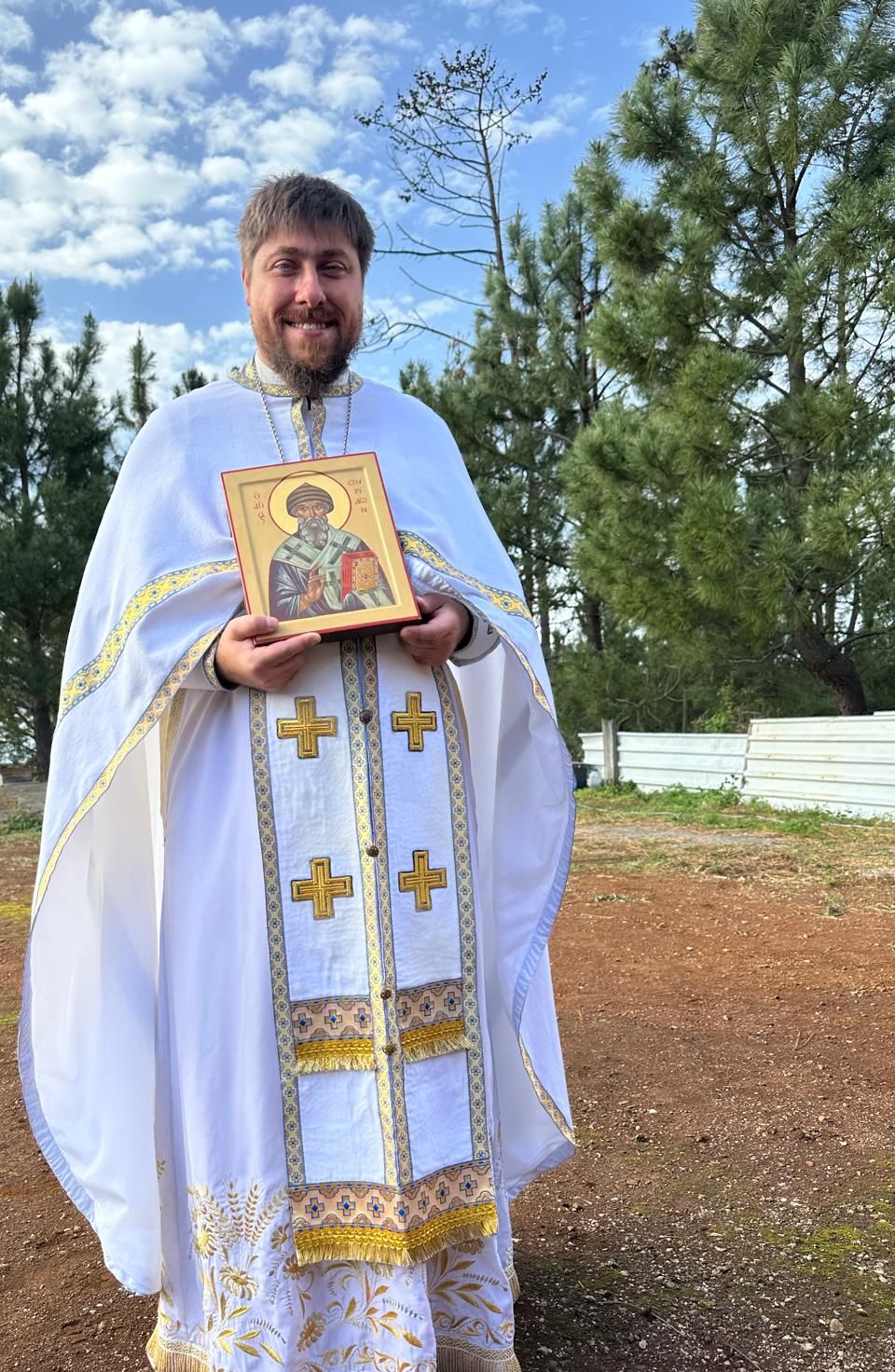 Father Pavel in white vestments holding an icon of Saint Spyridon